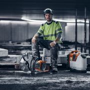 Construction worker sitting on concrete blocks with a power cutter and a water tank nearby.