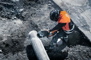 Trabalhador da construção civil usando um cortador de energia em um cano de concreto em um canteiro de obras.