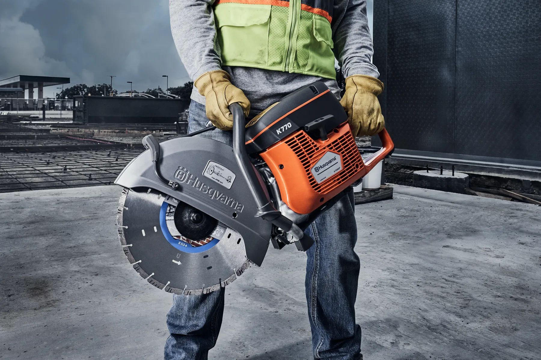 Ouvrier du bâtiment tenant une découpeuse Husqvarna K770 avec une lame diamant sur un chantier en béton.