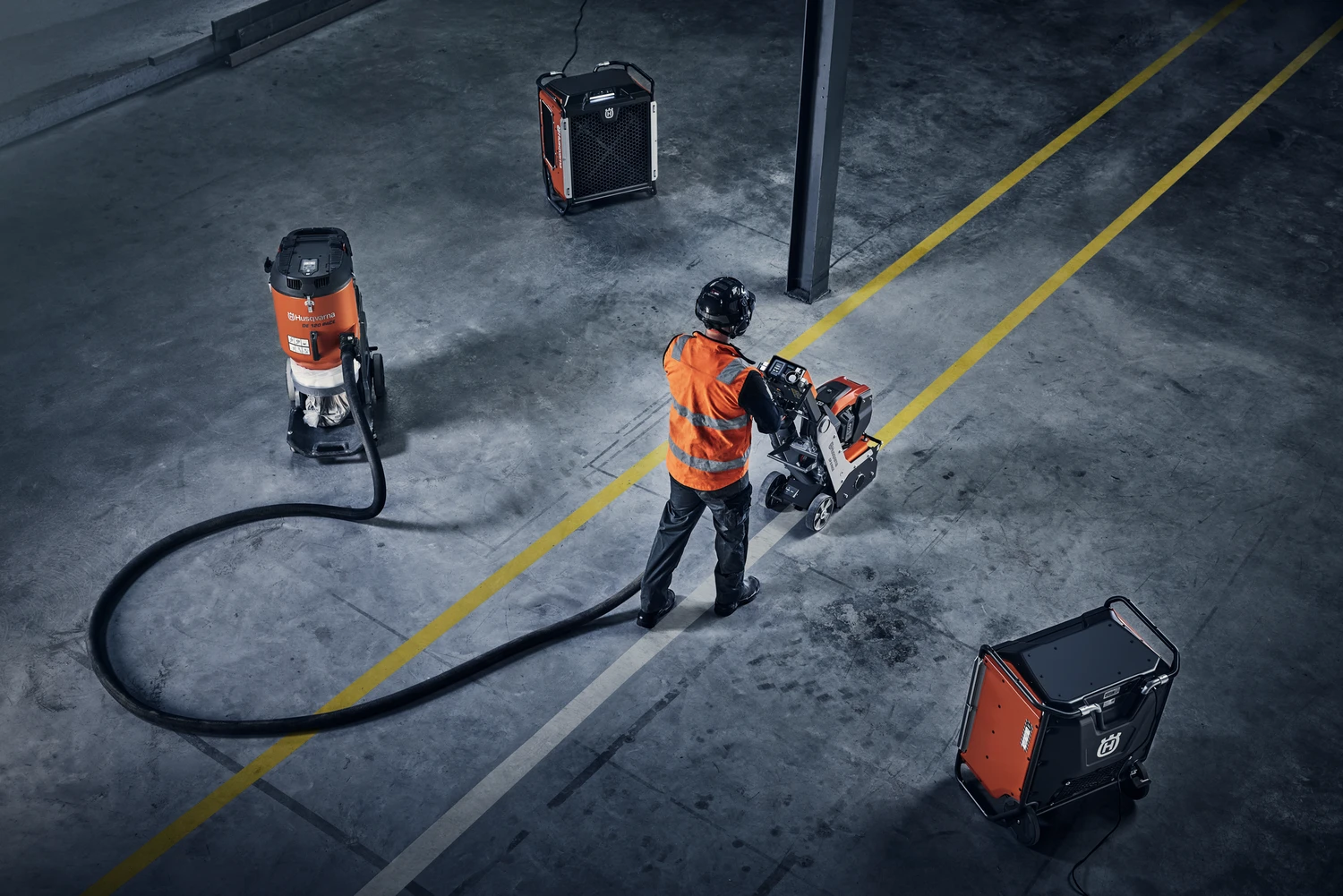 Construction worker operating a floor grinder indoors with connected dust extractor units.