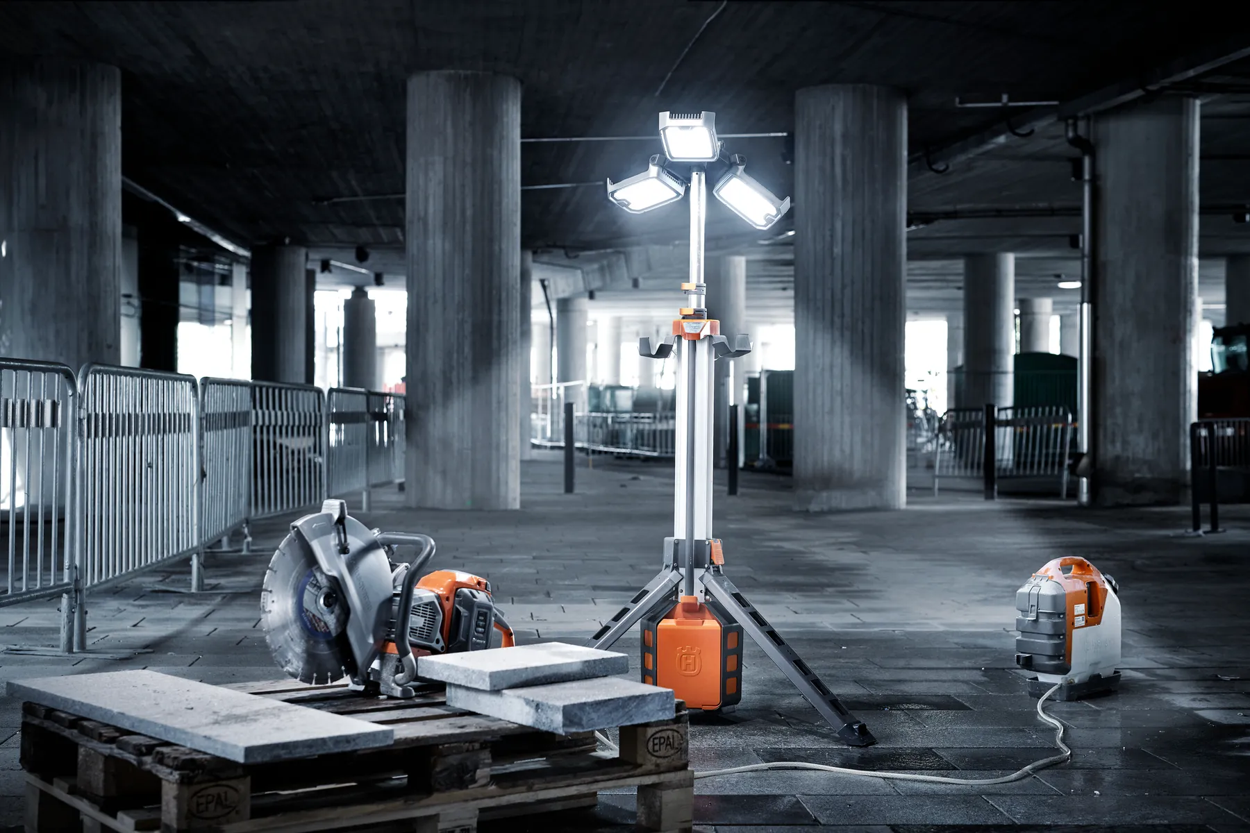 Șantier de construcții cu un tăietor electric, lampă de lucru și aspirator pe o podea de beton.